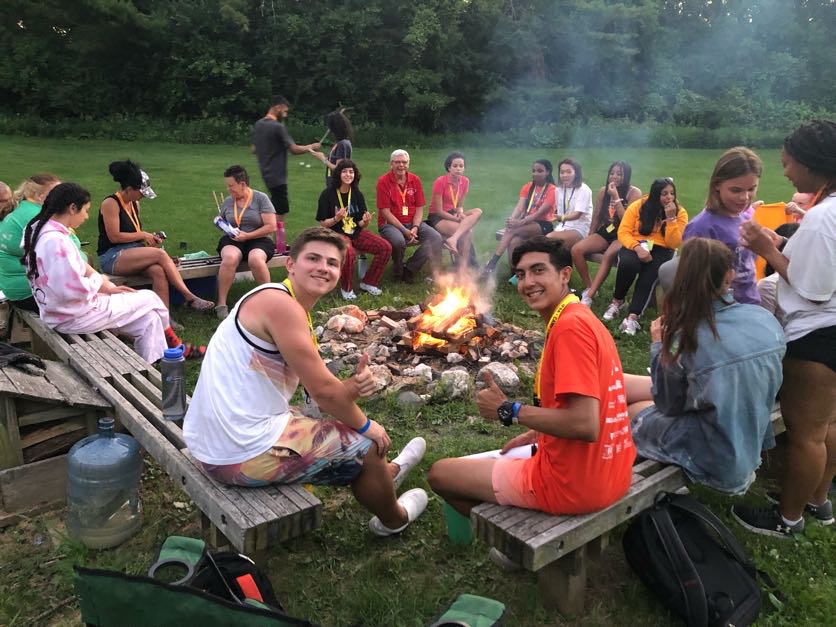 Large group of campers and counselors sitting around a bonfire