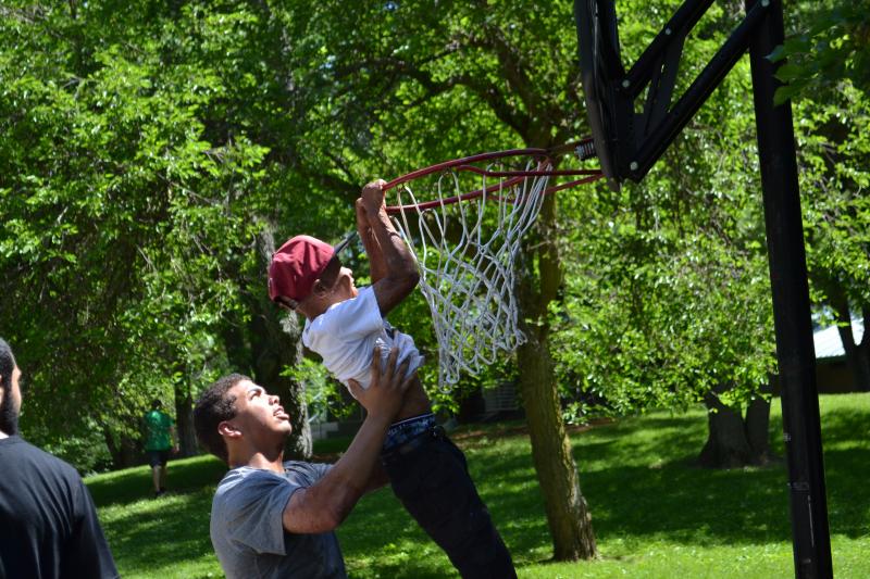 Camp counselor holding up young camper to hang from a basketball hoop