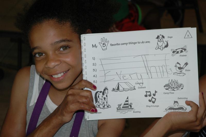A young girl displays her camp diary with a smile