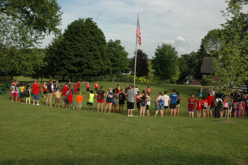 Campers gather on a grassy field to raise the American flag
