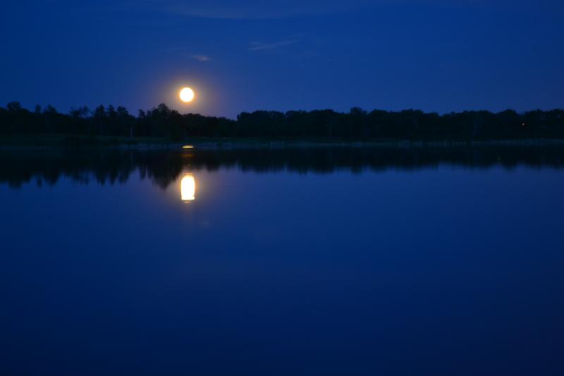 Full moon at night over a moonlit lake surrounded by forest