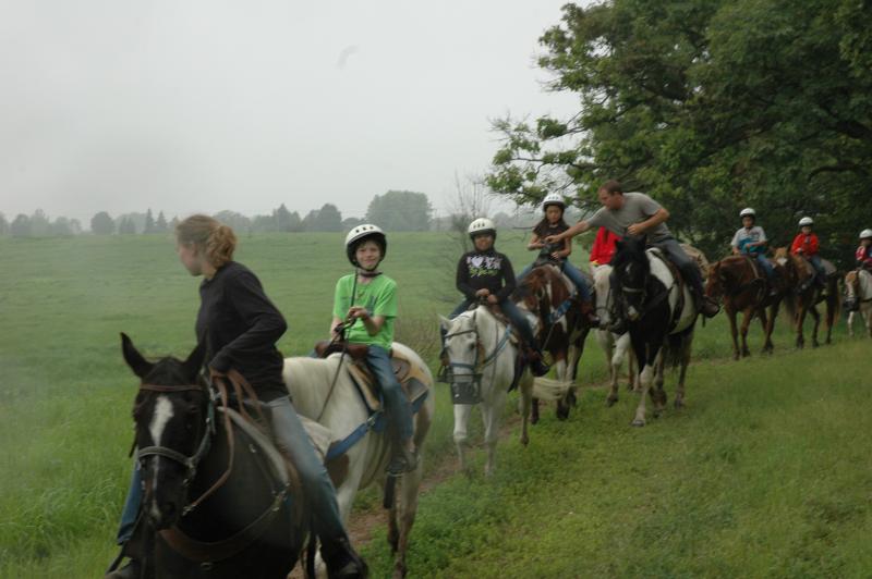 A group of campers riding horses in a line along a misty trail