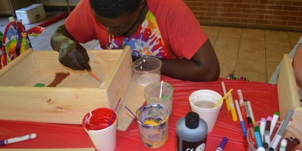 Camper painting a wooden box at an arts and crafts table