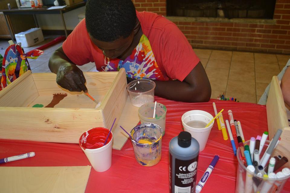 Camper painting a wooden box at an arts and crafts table