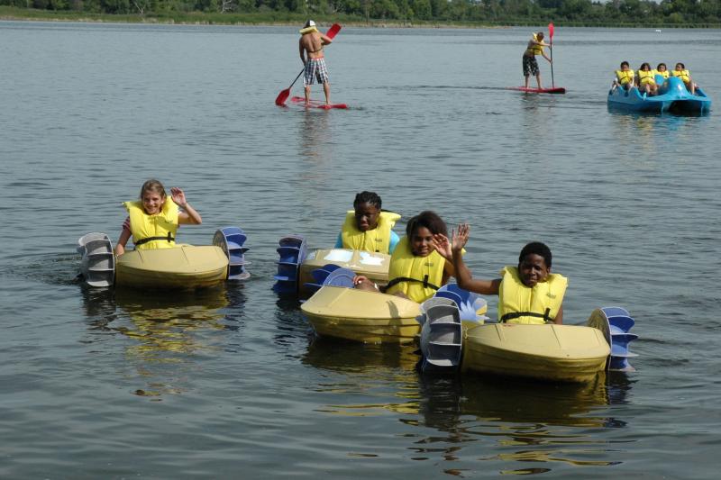 Campers in bright yellow life preservers paddleboating on the lake