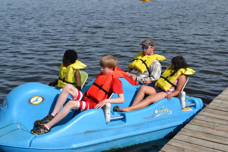 campers in life preservers learning to ride a bright blue paddleboat on the lake