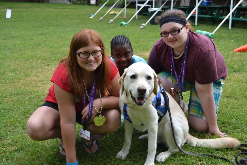 Three young campers pose with a camp therapy dog wearing a blue vest