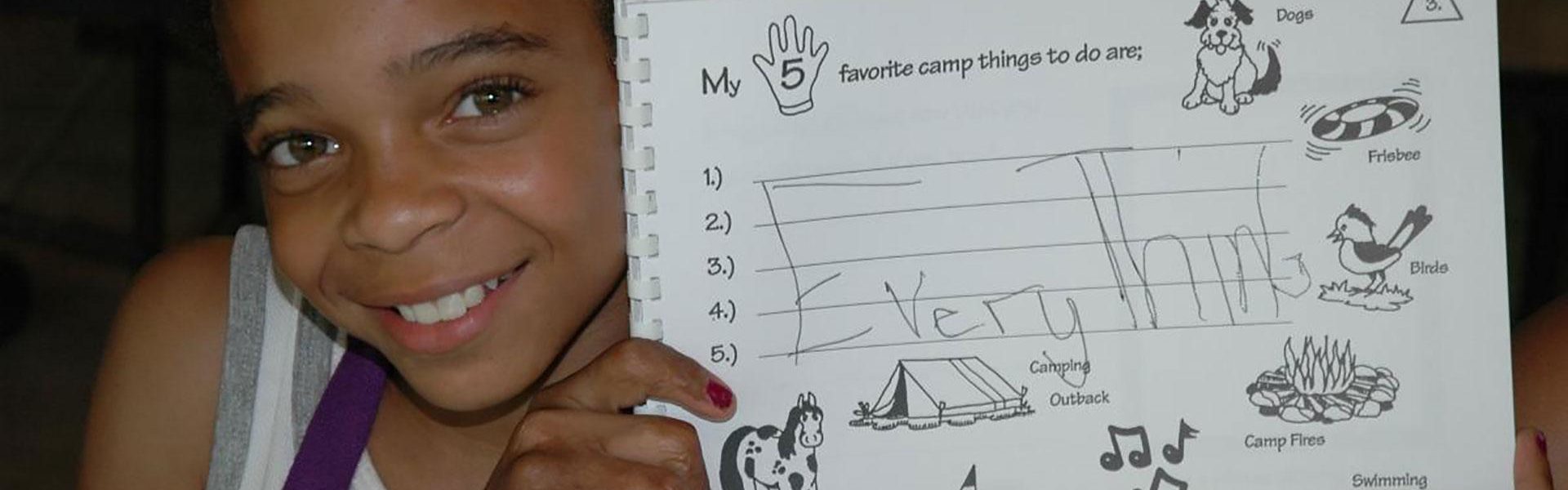 Young girl holding up activity book page the says "My 5 favorite camp things to do are: EVERYTHING"