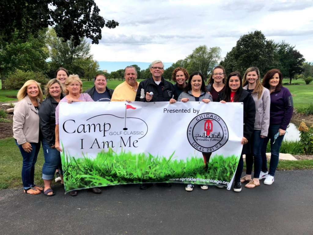 Group holding up Camp I Am Me Golf Classic Banner